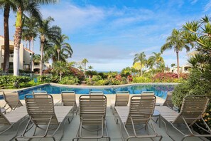 A poolside area with lounge chairs and a pool surrounded by palm trees and greenery.