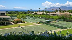 A tennis court with a view of a mountain and a building with a covered seating area. - Palms at Wailea #205 Fully Remodeled, Ground Floor Unit, Shared Hot Tub, A/C (Wailea)