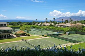 A tennis court with a view of a mountain and a building with a covered seating area.