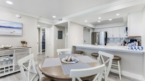 A modern kitchen with white cabinets, a stainless steel refrigerator, and a bar area with stools. - SUNDIAL A306 - Direct Beachfront Sanibel Condo (Sanibel)