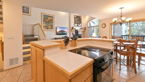 A modern kitchen with a central island, a dining area with wooden chairs, and a staircase leading to another level. - Chimney Ridge Sunflower Townhome: Walk to Lift, Private Hot Tub (Breckenridge)
