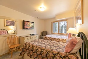 A bedroom with two beds, a chair, a desk, and a window.