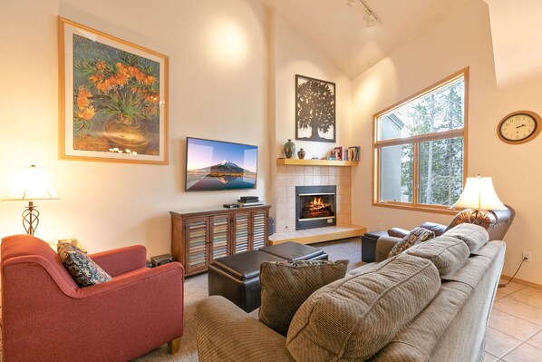 A living room with a sofa, armchair, and a fireplace. There is a television and a bookshelf.