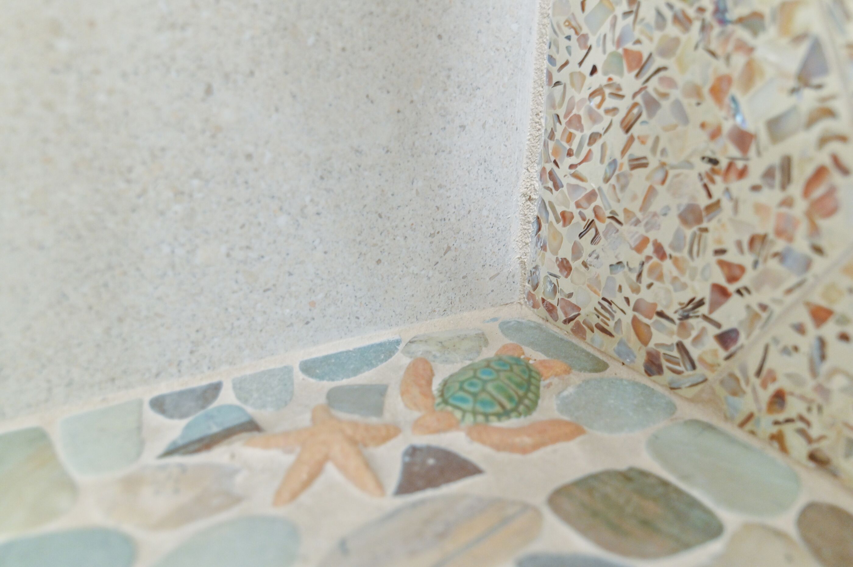 A corner of a room with a mosaic tile floor featuring sea creatures and a plain wall.
