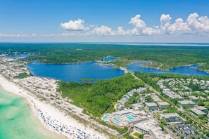 An aerial view of a coastal resort with multiple swimming pools, a beach, and a dense forested area.