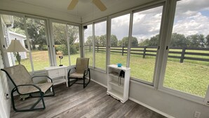 A sunroom with a ceiling fan, a desk, two chairs, and a view of a grassy yard with a wooden fence. - Relaxation & Privacy w/Golf Cart Conveniently Located NOW Waiting for YOU! (The Villages)