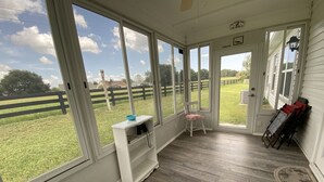 A room with large windows, a wooden floor, a white bench, and a chair with a pink cushion. - Relaxation & Privacy w/Golf Cart Conveniently Located NOW Waiting for YOU! (The Villages)