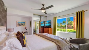 Ein Hotelzimmer mit Bett, Sessel, Deckenventilator, Fernseher und einem Fenster mit Vorhängen.