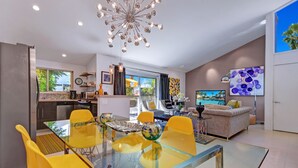 Ein modernes Wohnzimmer mit einem Glastisch, gelben Stühlen und einer großen Kronleuchter.