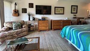 Una habitación con cama, sofá, escritorio, televisor y guitarra.