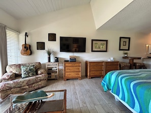 Una stanza con un letto, un divano, una scrivania, una televisione e una chitarra.