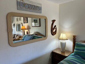 A bedroom with a bed, a nightstand with a lamp, a wall-mounted mirror, and a decorative piece.