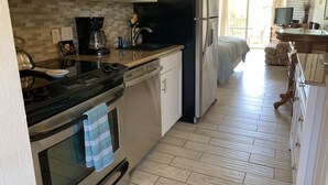 Una cocina compacta con microondas, estufa y refrigerador. Cuenta con un rebozo de azulejos, piso de madera y un pequeño comedor con sofá.