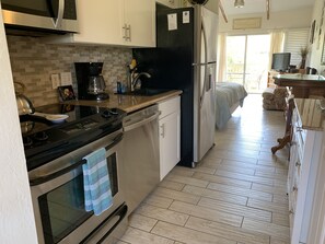 Una cucina compatta con forno a microonde, piano cottura e frigorifero. Dispone di una parete rivestita in piastrelle, pavimento in legno e un piccolo angolo ristoro con divano.