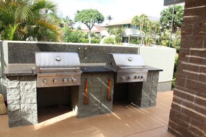 Area barbecue esterna con due griglie a gas, banconi in pietra e parete di fondo in pietra.