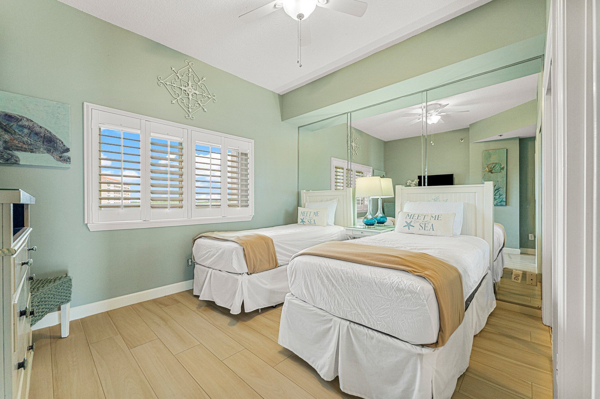 A bedroom with two beds, a large mirror, and a window with shutters.