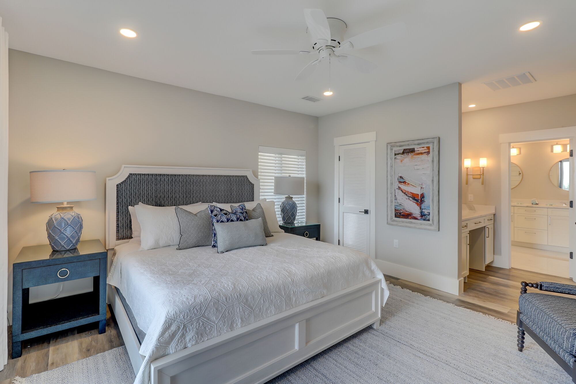 A bedroom with a large bed, bedside tables, a ceiling fan, and a bathroom with a mirror and sink.