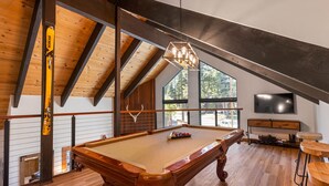Une table de billard dans une pièce avec des poutres en bois, une grande fenêtre et un téléviseur.