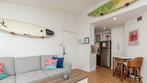 A modern living room with a grey sofa, a wooden coffee table, and a surfboard on the wall. - Cozy Pet-Friendly Studio with Balcony & Lake Views (Corpus Christi)