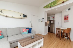 A modern living room with a grey sofa, a wooden coffee table, and a surfboard on the wall.