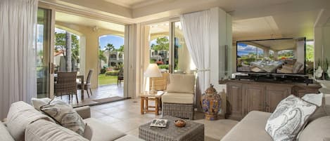 A spacious living room with a large sofa, a television, and a view of a garden through glass doors.