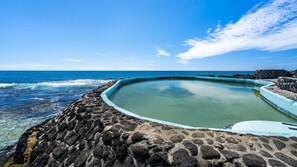 Ein kreisförmiger Pool mit Steinrand, umgeben von einer felsigen Küstenlinie und dem Meer.