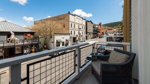 A balcony with wicker furniture, a view of a street with buildings, and a clear blue sky.