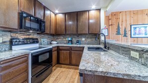 A kitchen with wooden cabinets, granite countertops, a built-in microwave, stove, and a coffee maker. - Upgraded, Light-Filled St. Moritz Villa 325 (Mammoth Lakes)