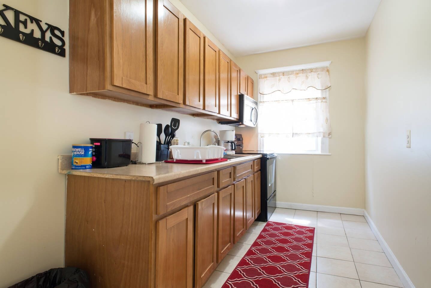 A compact kitchen with wooden cabinets, a microwave, and a red patterned rug.