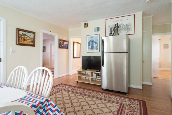 A modern kitchen with a refrigerator, dining table, chairs, and a TV.
