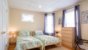 Een slaapkamer met twee bedden, een dressoir, een raam met gordijnen, een lamp en een ingelijste foto aan de muur.