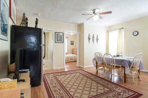 A living room with a black entertainment unit, a dining area with a table and chairs, a patterned rug, and a ceiling fan.