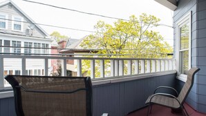 Een balkon met twee rieten stoelen en uitzicht op een boom met gele bladeren.