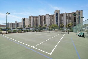 A tennis court with a net, surrounded by a fence, and a bench.
