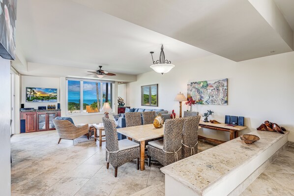 A spacious living area with a dining table, comfortable seating, a kitchen with a view, and a ceiling fan.