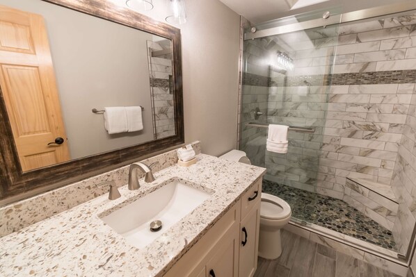 Bagno con lavabo su piano in granito, box doccia in vetro e porta in legno.