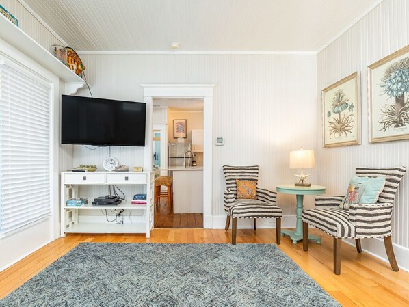 Ein Wohnzimmer mit Fernseher, zwei gestreifte Stühle, einem kleinen Tisch mit Lampe und einem Teppich.