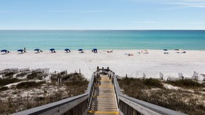 A wooden boardwalk leading to a beach with umbrellas and people relaxing.