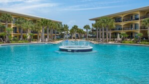 A large outdoor swimming pool surrounded by palm trees and yellow buildings with balconies.
