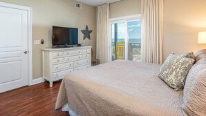 A bedroom with a bed, a dresser, a television, a ceiling fan, and a view of the outdoors. - Bay View Villas 203 | Waterfront, Community Pool (Tybee Island)
