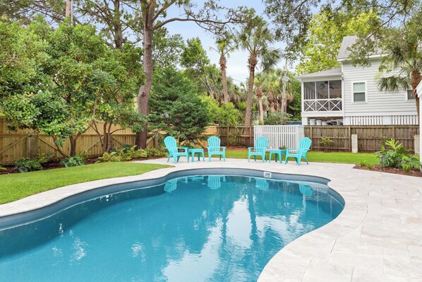 A backyard with a swimming pool, green chairs, and a wooden fence. - Butler Beach Cottage | Pet-Friendly, Quiet Neighborhood (Tybee Island)