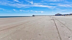 A beach with a long pier extending into the ocean, a clear sky, and a few buildings in the distance. - Butler Beach Cottage | Pet-Friendly, Quiet Neighborhood (Tybee Island)