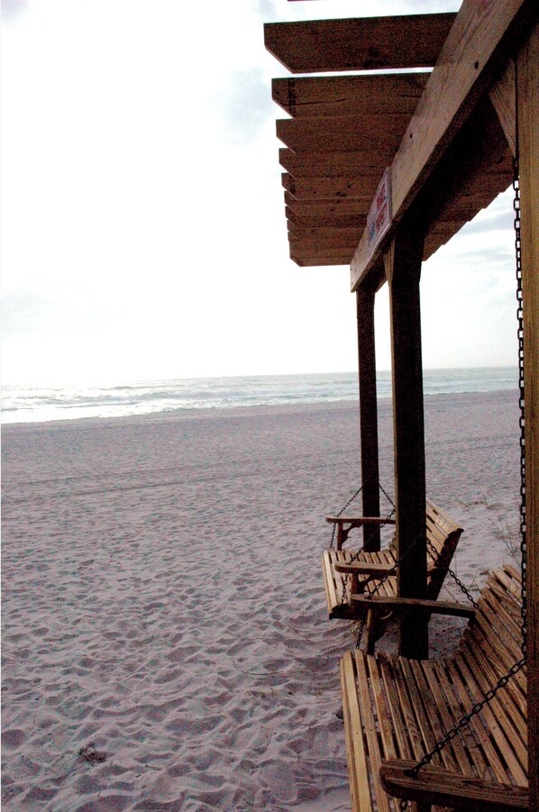 Un banco de madera en la playa con respaldo de malla metálica, con vista al océano.