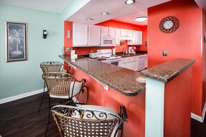 A kitchen with white cabinets, a granite countertop, and a red accent wall.