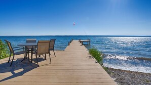 Une jetée en bois mène à une côte rocheuse. Une table et des chaises se trouvent sur le côté gauche.