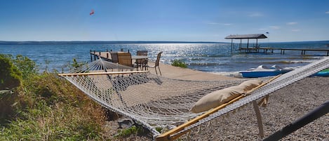 Una hamaca en una playa pedregosa, con vista al agua y un muelle.