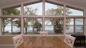 Une pièce dotée de grandes fenêtres donnant sur un lac, d’un plancher en bois et d’une petite table avec des chaises.