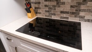 Una cocina con tope de inducción negro, un bloque de cuchillos y salpicadero de azulejos.