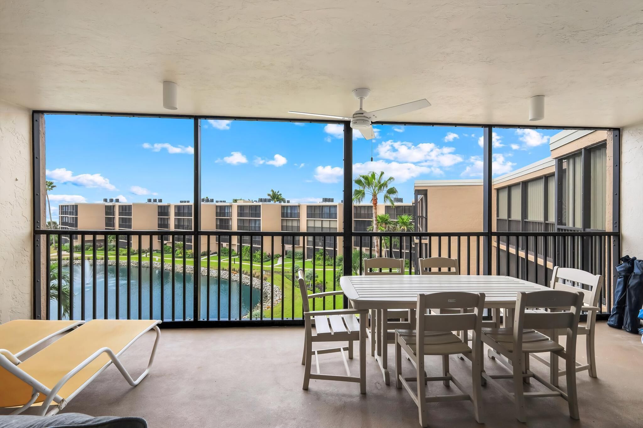 A balcony with a table and chairs, a view of a swimming pool, and a building complex in the background.