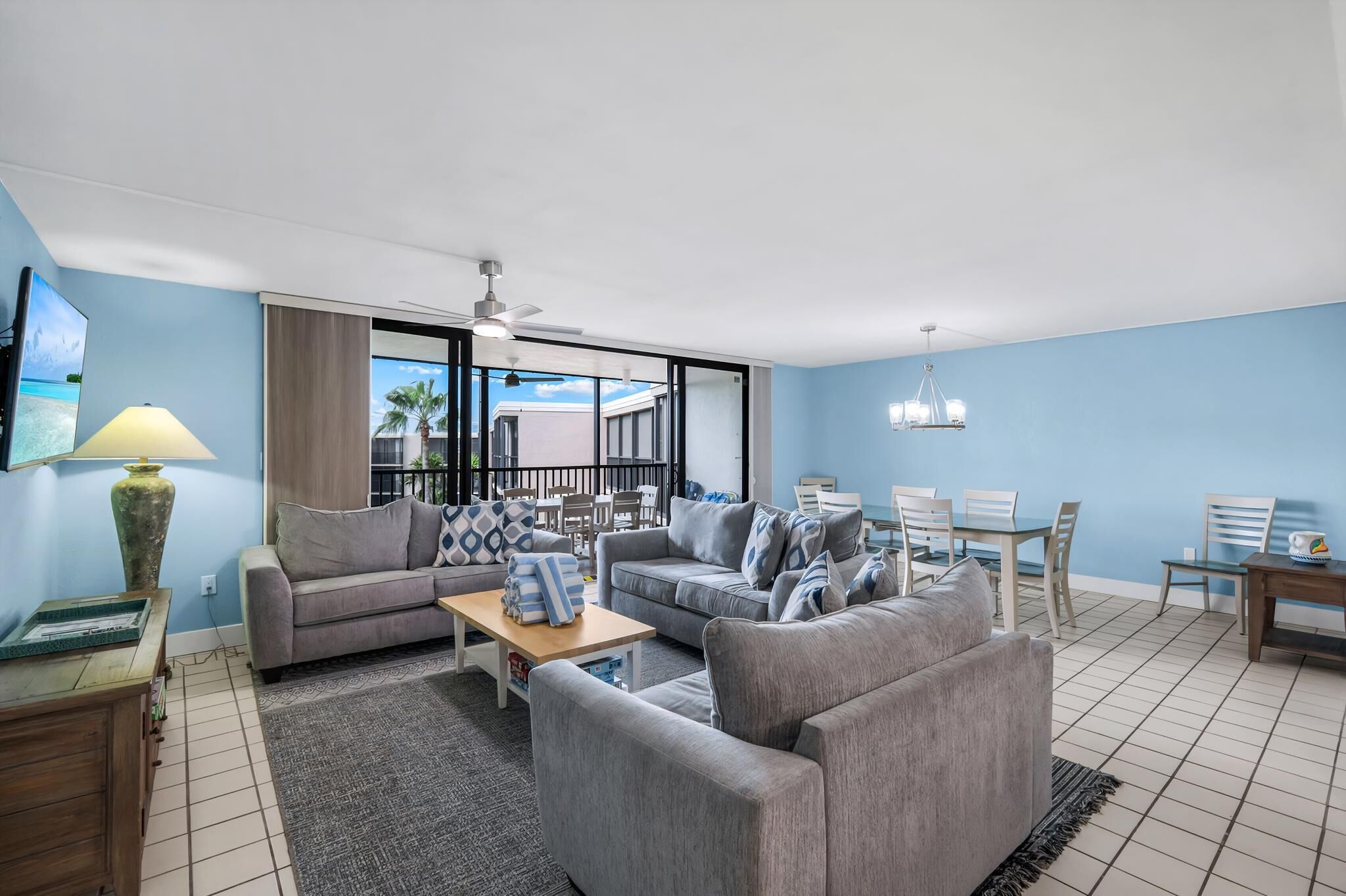 A modern living room with grey sofas, a wooden coffee table, and a dining area with white chairs.